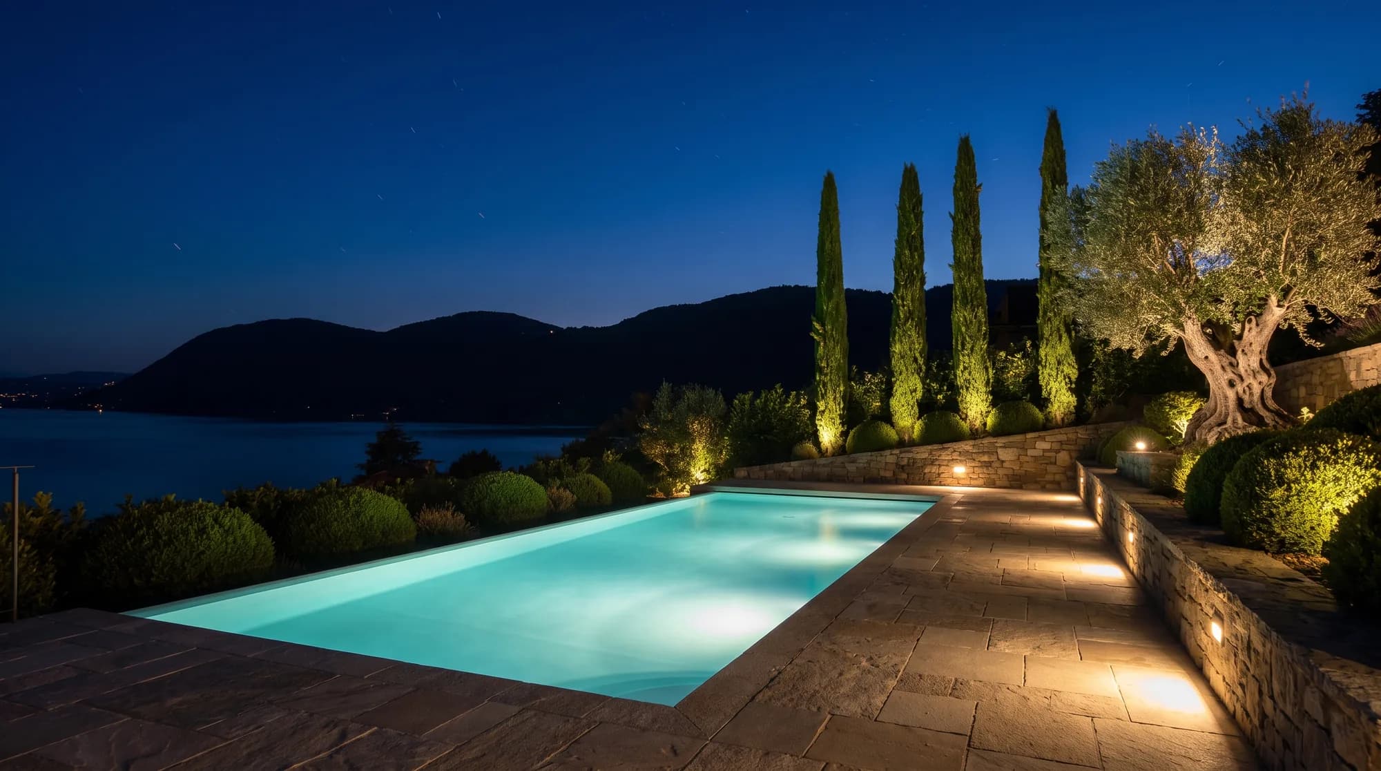 Piscine éclairée de nuit face au lac, terrasse en pierre naturelle